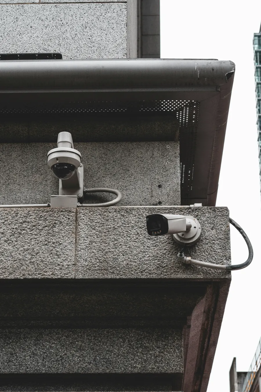 A dome camera and a bullet camera mounted under the eaves of a stone building