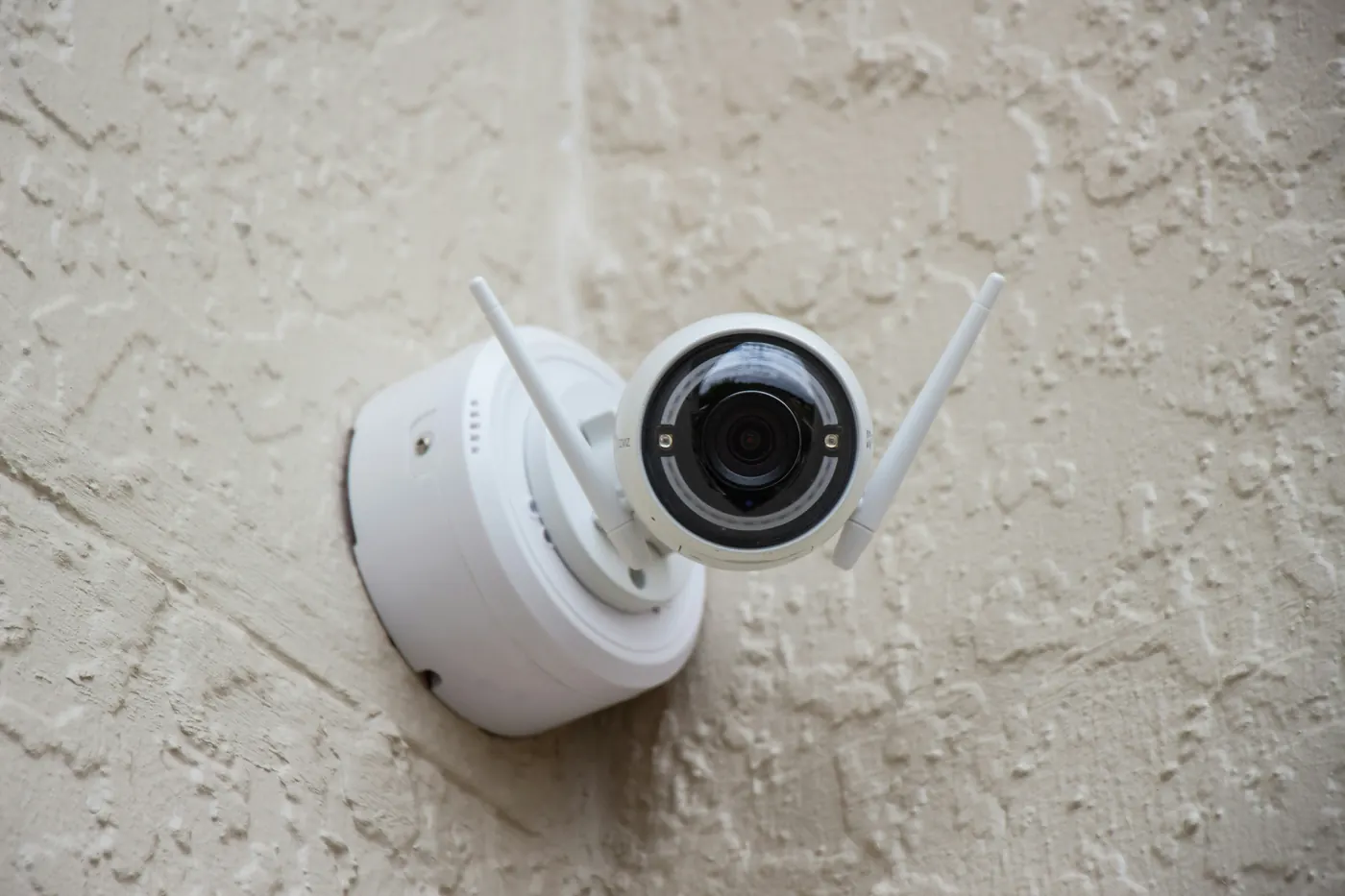 White wireless dome camera with two antennas mounted on a rendered exterior wall